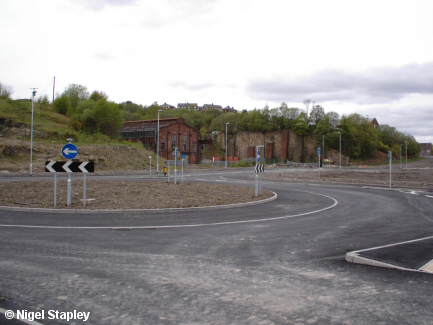 Picture of a roundabout on a new road with old industrial buildings in the background