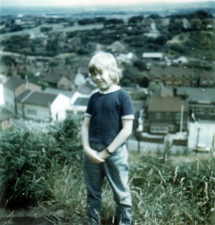 Photo of a boy standing with part of a village behind and below him