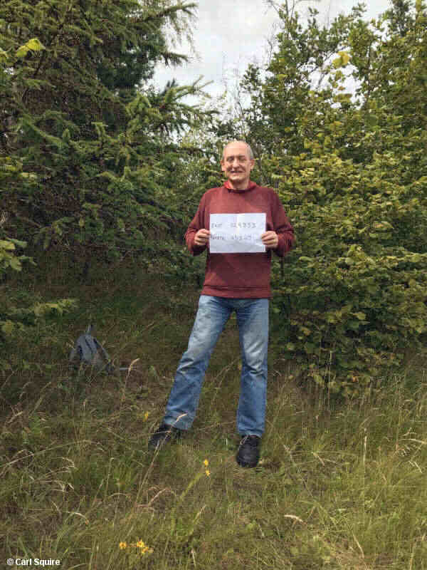 Picture of a man in undergrowth holding a piece of paper with a map reference on it
