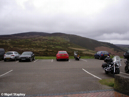 Photo across a small car park towards a large hill