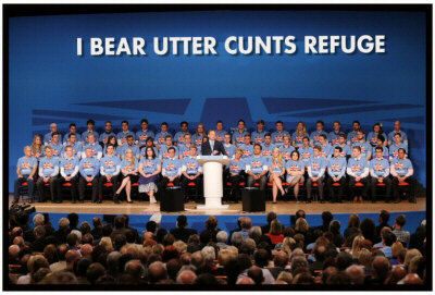 Photo of Tory Party rally with group of identically-dressed people with the backdrop slogan amended to 'I Bear Utter Cunts Refuge'